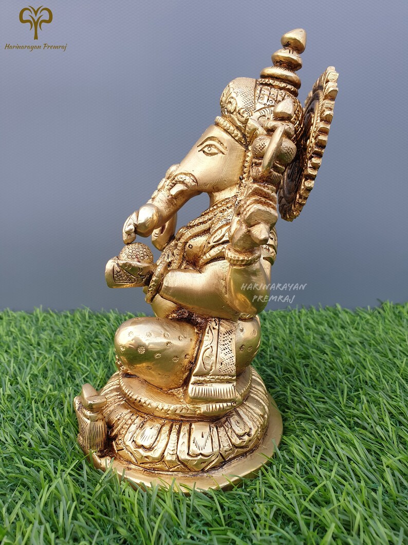 Puede incluir: Una estatua de bronce dorada de Ganesha, el dios hind&uacute; de la sabidur&iacute;a y la prosperidad, sentado sobre una base de loto. La estatua est&aacute; intrincadamente detallada con tallas ornamentadas y una corona en la cabeza de Ganesha.