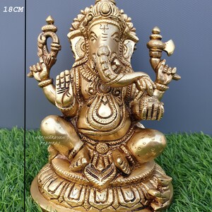 Puede incluir: Una estatua de bronce dorado de Ganesha, el dios hind&uacute; de la sabidur&iacute;a y la prosperidad, sentado sobre una base de loto. La estatua mide 18 cm de alto y 15 cm de ancho.