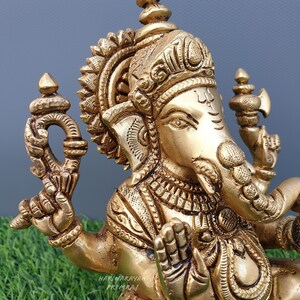 Puede incluir: Una estatua de metal dorado de Ganesha, el dios hind&uacute; de la sabidur&iacute;a y la prosperidad. La estatua est&aacute; intrincadamente detallada con tallas ornamentadas y una corona. Ganesha est&aacute; representado sentado con su trompa levantada y su mano derecha en un gesto de bendici&oacute;n.