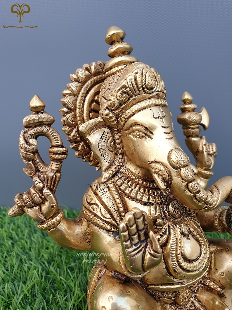 Puede incluir: Una estatua de metal dorado de Ganesha, el dios hind&uacute; de la sabidur&iacute;a y la prosperidad. La estatua est&aacute; intrincadamente detallada con tallas ornamentadas y una corona. Ganesha est&aacute; representado sentado con su trompa levantada y su mano derecha en un gesto de bendici&oacute;n.
