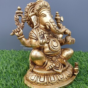 Puede incluir: Una estatua de metal dorada de Ganesha, el dios hind&uacute; de la sabidur&iacute;a y la prosperidad, sentado sobre una base de loto. La estatua est&aacute; intrincadamente detallada y presenta un dise&ntilde;o tradicional.