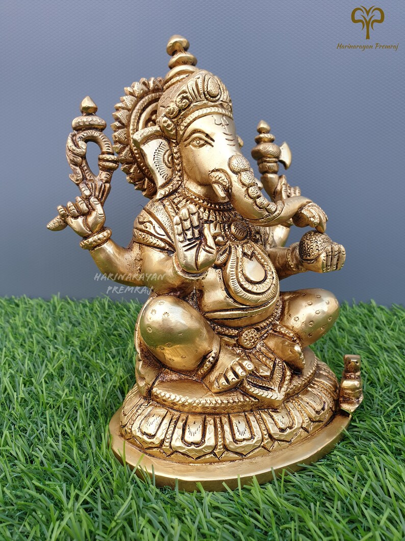 Puede incluir: Una estatua de metal dorada de Ganesha, el dios hind&uacute; de la sabidur&iacute;a y la prosperidad, sentado sobre una base de loto. La estatua est&aacute; intrincadamente detallada y presenta un dise&ntilde;o tradicional.