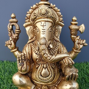 Puede incluir: Una estatua de metal dorada de Ganesha, el dios hind&uacute; de la sabidur&iacute;a y la prosperidad. La estatua est&aacute; intrincadamente detallada y presenta a Ganesha sentado en un trono de loto con su trompa levantada y sosteniendo un dulce modaka en su mano.