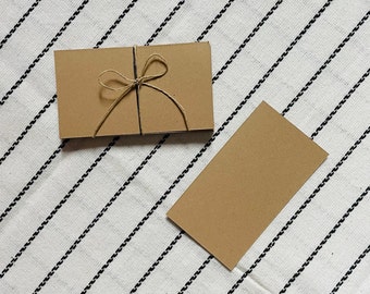 May include: Two brown kraft paper cards on a white and black striped fabric background. One card is tied with twine and has a bow.