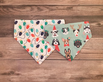 May include: Two dog bandanas with Christmas themes. One bandana is white with a pattern of red and green Christmas lights. The other bandana is green with a pattern of dogs wearing Christmas hats, reindeer antlers, and other festive accessories.