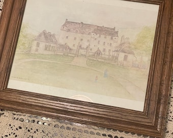 May include: A framed watercolor painting depicting a large stone manor house with a gated entrance, surrounded by green lawns and trees. The artwork is enclosed in a medium-brown wooden frame with a textured finish and visible wood grain patterns.