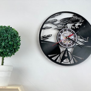 Può includere: Un orologio in vinile nero con la silhouette della Starship Enterprise di Star Trek. L'orologio ha un quadrante bianco con numeri neri e una lancetta dei secondi rossa.