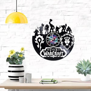 Puede incluir: Reloj de vinilo negro con personajes y logotipo de World of Warcraft. El reloj tiene un fondo negro con un dise&ntilde;o de galaxia en el centro. Las manecillas del reloj son negras y blancas.