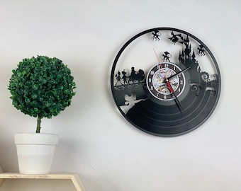 May include: Black vinyl record clock featuring a silhouette design of a group of people walking across a bridge with a castle in the background. The clock face has Roman numerals and a red second hand.