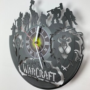 Puede incluir: Un reloj de vinilo negro con un dise&ntilde;o de World of Warcraft. La esfera del reloj es blanca con n&uacute;meros romanos negros y una aguja de reloj negra y blanca. El dise&ntilde;o incluye una cabeza de le&oacute;n y varias figuras del juego.