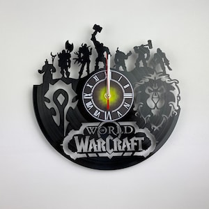 Puede incluir: Reloj de vinilo negro con personajes del videojuego World of Warcraft. La esfera del reloj tiene n&uacute;meros romanos y un dise&ntilde;o en blanco y negro. El reloj est&aacute; rodeado de personajes del juego, incluyendo un le&oacute;n, un guerrero y un mago.