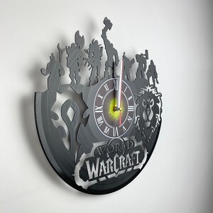 Puede incluir: Un reloj de vinilo negro con personajes del videojuego World of Warcraft. La esfera del reloj es blanca con n&uacute;meros romanos negros y agujas negras. El reloj est&aacute; rodeado de siluetas de personajes del juego, incluyendo un guerrero, un mago y un p&iacute;caro. El reloj tambi&eacute;n est&aacute; decorado con el logotipo de World of Warcraft.