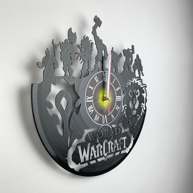 Puede incluir: Un reloj de vinilo negro con personajes del videojuego World of Warcraft. La esfera del reloj es blanca con n&uacute;meros romanos negros y agujas negras. El reloj est&aacute; rodeado de siluetas de personajes del juego, incluyendo un guerrero, un mago y un p&iacute;caro. El reloj tambi&eacute;n est&aacute; decorado con el logotipo de World of Warcraft.
