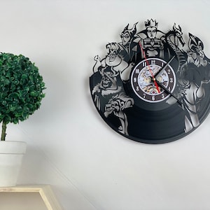 Op de afbeelding: Zwarte vinyl platen klok met Disney-schurken, waaronder Maleficent, Ursula, Cruella de Vil en de Evil Queen. De klok heeft een zwarte achtergrond met witte contouren van de schurken. Het klokje is wit met zwarte cijfers en wijzers.