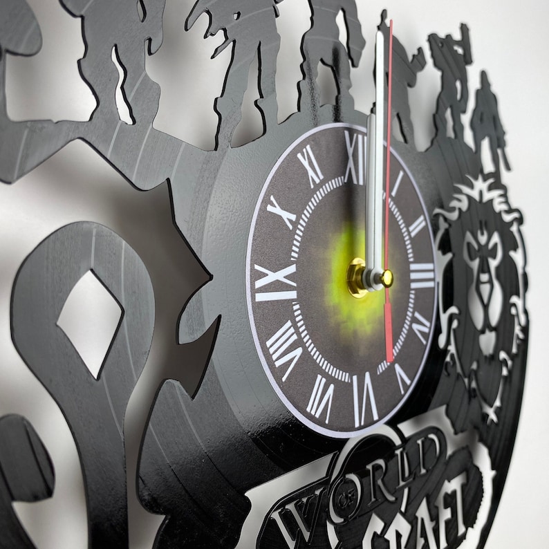 Puede incluir: Reloj de vinilo negro con una silueta de personajes del videojuego World of Warcraft. La esfera del reloj tiene n&uacute;meros romanos y un centro dorado. El reloj est&aacute; decorado con las palabras "World of Warcraft".