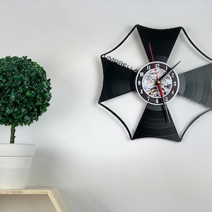 Op de afbeelding: Een zwarte en witte vinyl platenspeler klok in de vorm van het Umbrella Corporation logo uit de Resident Evil videogame serie. De wijzerplaat van de klok heeft een tandwielachtig ontwerp met Romeinse cijfers voor de uren.
