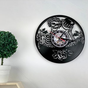 May include: Black vinyl record clock featuring a skeleton with a flower crown and a rose design. The clock face has Roman numerals and a skeleton key design.