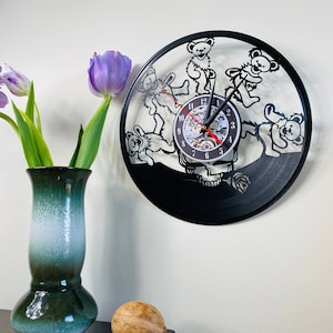 May include: A black vinyl record clock featuring a skull with five dancing bears. The clock has a red second hand and a white face with black numbers.