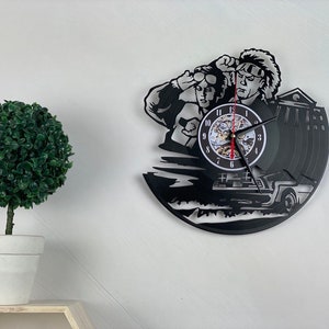 May include: Black vinyl record clock featuring a silhouette of two characters from the movie Back to the Future, a DeLorean time machine, and a clock face with Roman numerals.