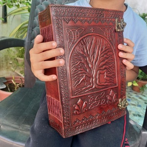 May include: A dark red leather journal with an embossed tree of life design. The journal features Celtic knotwork and a metal clasp. The spine has decorative stitching. A unique, vintage-style notebook, ideal for writing.
