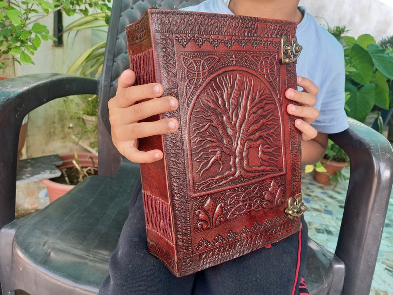 May include: A dark red leather journal with an embossed tree of life design. The journal features Celtic knotwork and a metal clasp. The spine has decorative stitching. A unique, vintage-style notebook, ideal for writing.