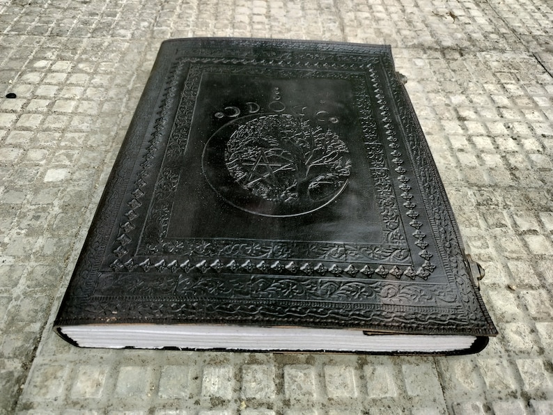 May include: A black leather-bound journal with an embossed design of a tree and a pentagram. The journal has a decorative border and a clasp.
