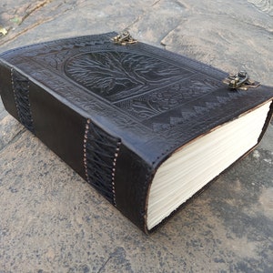 May include: Black leather journal with an embossed tree of life design on the cover. The journal has a clasp closure and stitched edges. The pages are cream-coloured.
