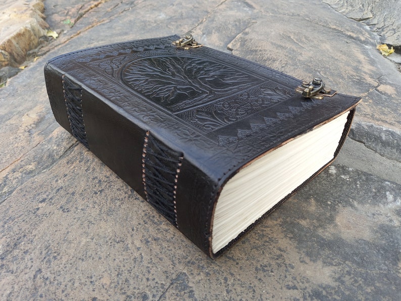 May include: Black leather journal with an embossed tree of life design on the cover. The journal has a clasp closure and stitched edges. The pages are cream-coloured.
