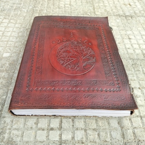 May include: A brown leather journal with a tree of life design and a pentacle symbol. The journal has a decorative border and is closed.