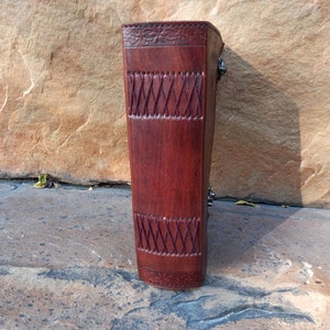 May include: A dark brown leather journal with embossed floral and geometric patterns. The journal is secured with metal clasps. The leather has a rich, textured appearance, suggesting quality craftsmanship. The journal is a classic design.
