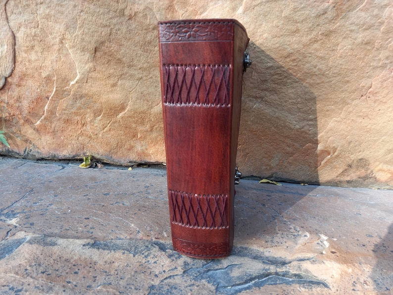 May include: A dark brown leather journal with embossed floral and geometric patterns. The journal is secured with metal clasps. The leather has a rich, textured appearance, suggesting quality craftsmanship. The journal is a classic design.