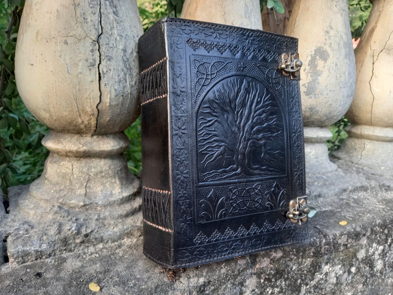 May include: Black leather journal with a tree of life design embossed on the cover. The journal has a metal clasp closure and decorative stitching along the spine. The cover features Celtic knotwork.