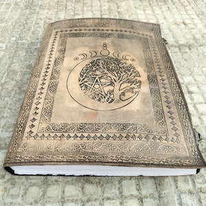 May include: A brown leather journal with a tree of life design and a pentacle inside a crescent moon. The journal has a decorative border and a clasp.