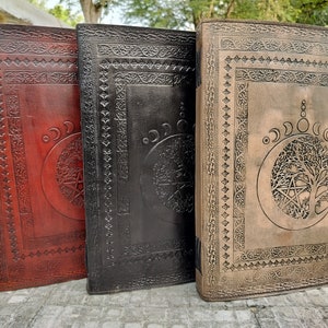 May include: Three leather-bound journals with embossed designs. The journals are red, black, and brown. Each journal features a tree of life design with a pentagram and moon phases.