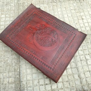 May include: A brown leather journal with an embossed tree of life design and a pentagram. The journal has a decorative border around the edges.