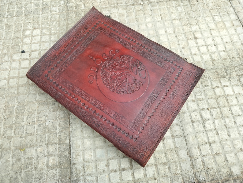 May include: A brown leather journal with an embossed tree of life design and a pentagram. The journal has a decorative border around the edges.
