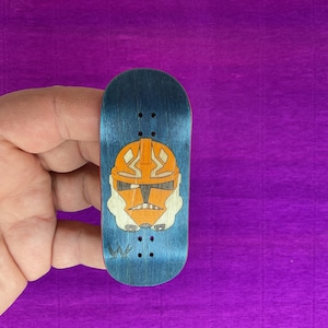 May include: A blue fingerboard with an orange and white helmet design. The miniature skateboard has a blue background with an orange helmet design in the center. The helmet has white accents and is a stylized illustration.