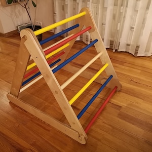 May include: Wooden climbing frame for children, featuring a triangular base with multiple rungs in yellow, blue, and red.