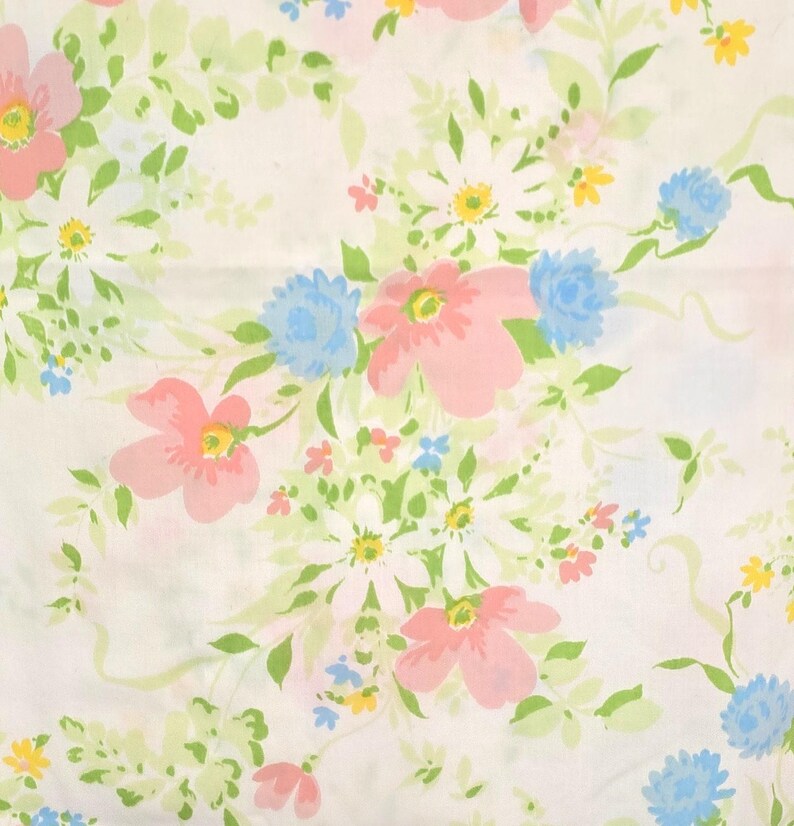 May include: A white fabric with a floral pattern featuring pink, blue, yellow, and white flowers. Green leaves and stems intertwine among the blooms. The design is a repeating pattern of various flower types.