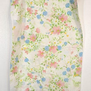 May include: A white fabric with a floral pattern featuring pink, blue, and yellow flowers, along with green leaves. The fabric is hanging from a clear plastic hanger.