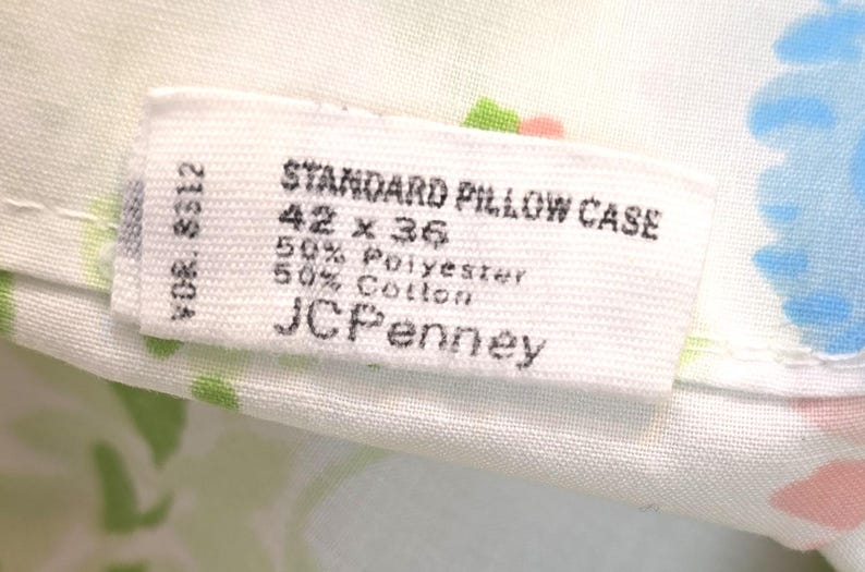May include: Close-up of a white pillowcase label with the text "STANDARD PILLOW CASE" and measurements of 42 x 36 inches. The label also indicates a 50% polyester and 50% cotton blend, with the JCPenney brand.