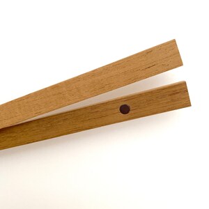 May include: Two wooden picture frame hanging rods with a black metal hanging clip. The rods are made of natural wood with a light brown finish.