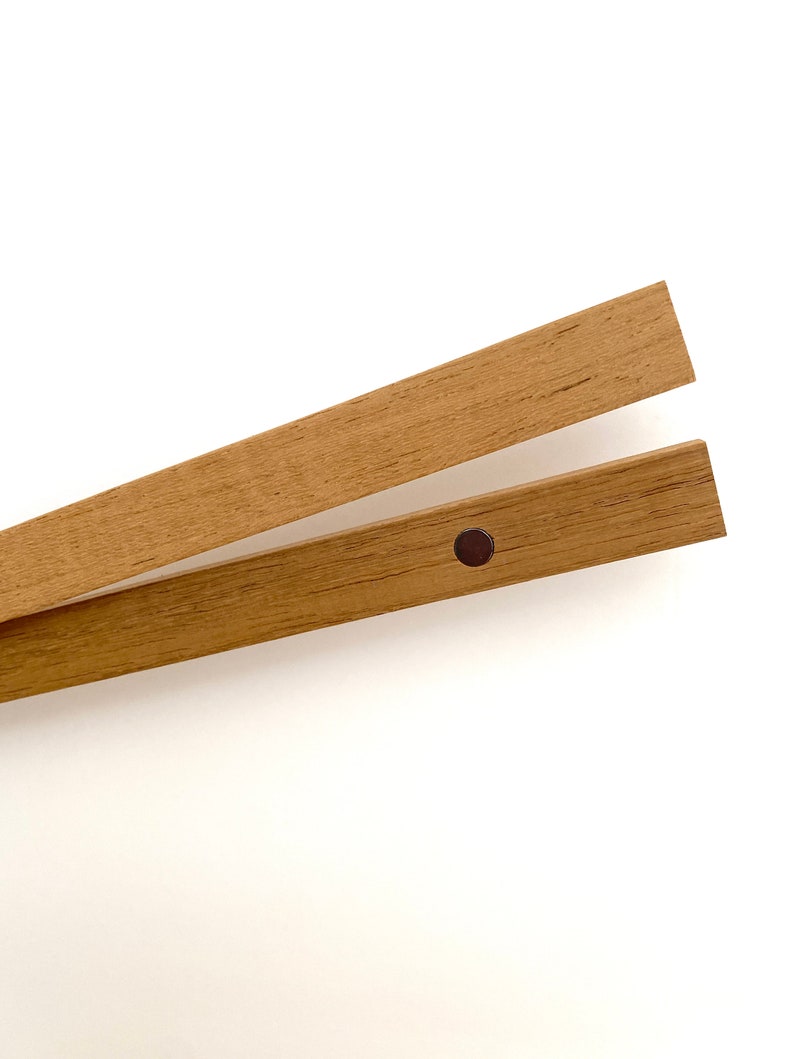 May include: Two wooden picture frame hanging rods with a black metal hanging clip. The rods are made of natural wood with a light brown finish.