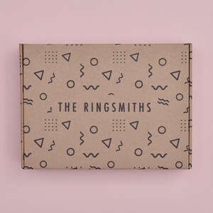 May include: A brown cardboard box with a geometric pattern and the text "THE RINGSMITHS" printed on it.