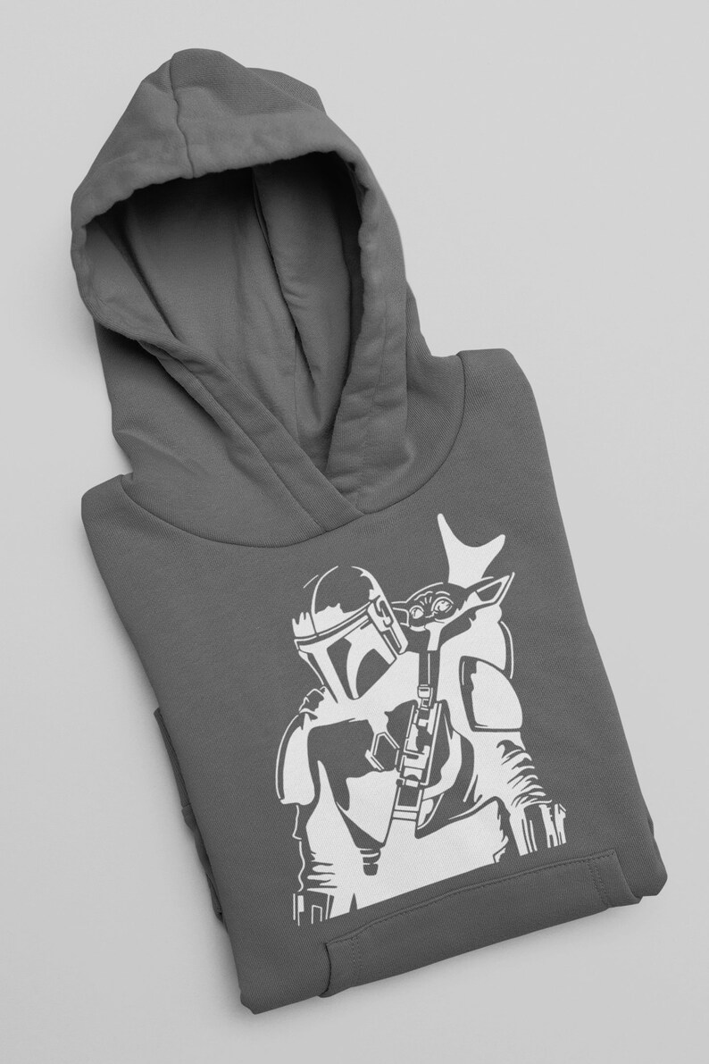 Puede incluir: Una sudadera con capucha gris con una silueta blanca de un personaje mandaloriano que lleva una peque&ntilde;a figura infantil en su hombro.