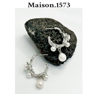 May include: A pair of silver hoop earrings with a textured, branch-like design. Each earring features a cluster of white pearls, including a larger pearl dangling from the bottom.