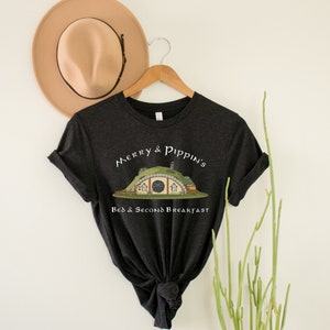May include: A dark gray t-shirt with a white graphic of a hobbit hole with the text "Merry & Pippin's Bed & Second Breakfast".