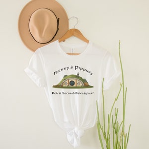 May include: White t-shirt with a graphic of a hobbit hole and the text "Merry & Pippin's Bed & Second Breakfast".
