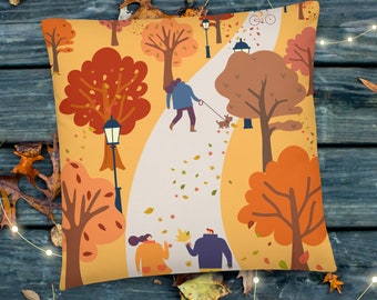 Puede incluir: Una almohada con una ilustración colorida de una escena de otoño. El diseño presenta un camino sinuoso a través de un parque con árboles, personas caminando y un perro con una correa. El fondo es de color amarillo-naranja con hojas que caen.