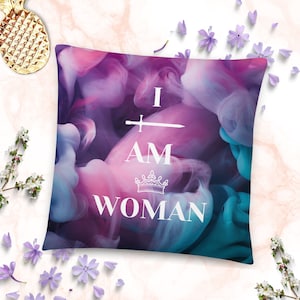 Può includere: Un cuscino astratto viola e blu con il testo "I AM WOMAN" in bianco con una grafica di spada e corona.